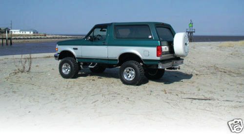 Green and silver 1993 Ford Bronco with spare tire on rear bumper, parked on beach