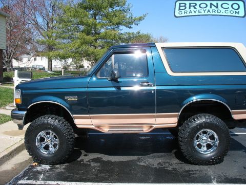 1993 Ford Bronco - Side view of a lifted 1993 Ford Bronco with custom chrome wheels and two-tone paint.
