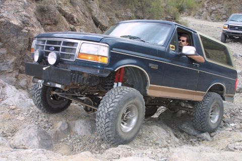1994 Ford Bronco - Modified Ford Bronco tackling a difficult rocky off-road path, with a second vehicle following behind.