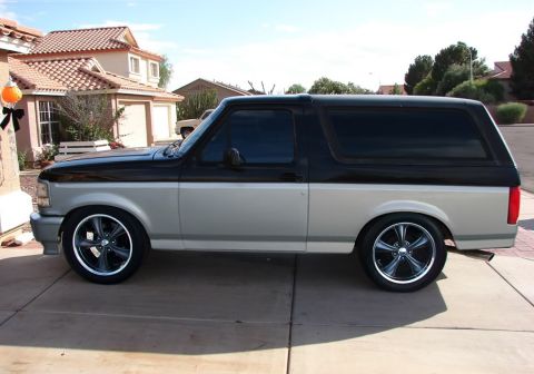 1993 Ford Bronco - Driver-side profile of a lowered two-tone black-over-silver full-size Ford Bronco slammed on large polished-lip five-spoke wheels with low-…