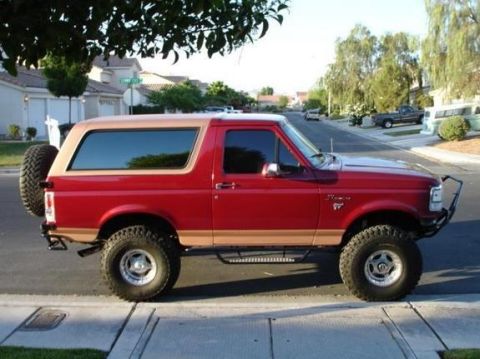 1993 Ford Bronco - Red over tan lifted full-size Ford Bronco with spare tire, parked in a suburban driveway, side profile.