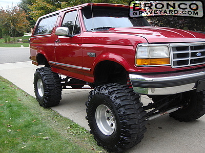 1993 Ford Bronco - Lifted red full-size Ford Bronco on a suspension lift with large Super Swamper-style mud tires on polished alloy wheels, parked on a reside…