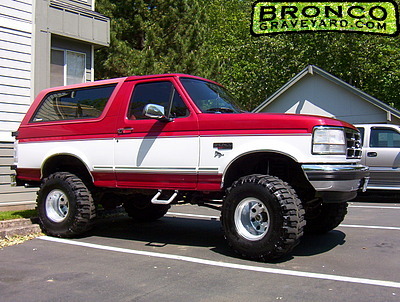 1993 Ford Bronco - Two-tone red over white full-size Ford Bronco with suspension lift and oversized mud-terrain tires, parked outdoors.