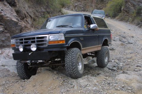 1994 Ford Bronco - A lifted 1994 Ford Bronco navigates a rough, rocky terrain with another vehicle following behind.