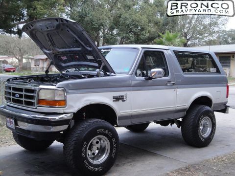 1993 Ford Bronco - two-tone silver lifted Ford Bronco with the hood raised, on chrome wheels and Trail tires; image watermarked BroncoGraveyard.com.