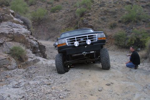1994 Ford Bronco - A black Ford Bronco navigates a challenging rocky terrain, with a man observing from the side.