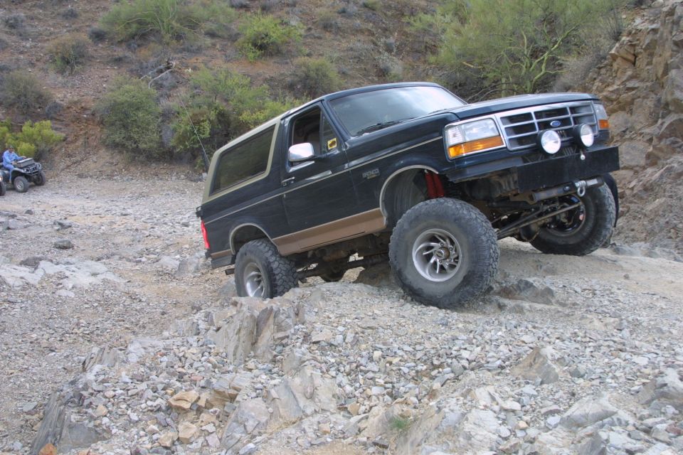 Black and tan lifted Ford Bronco flexing over rocky desert ledge