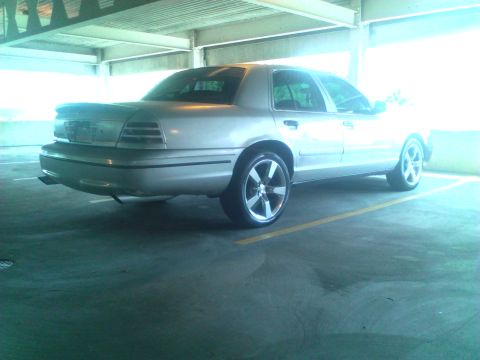 1999 Ford Crown Victoria - This 1999 Ford Crown Victoria is captured from a rear 3/4 angle, its silver paint and aftermarket wheels.