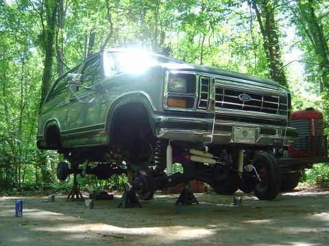 1986 Ford Bronco - 1986 Ford Bronco undergoing suspension work, lifted on jack stands in a wooded area.