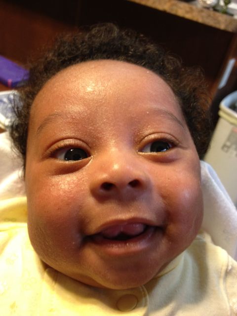 2010 Subaru Legacy - A baby smiles broadly, showing off a bit of tongue, in a close-up portrait.