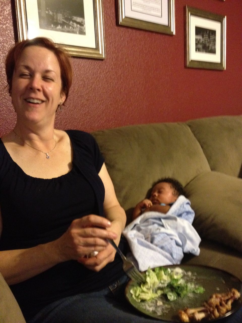 Woman laughing while a baby sleeps on a couch