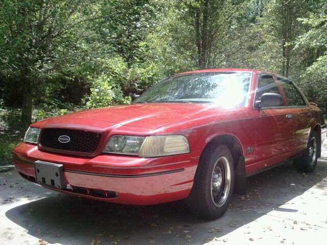 Red 2000 Ford Crown Victoria parked outdoors with trees in the background