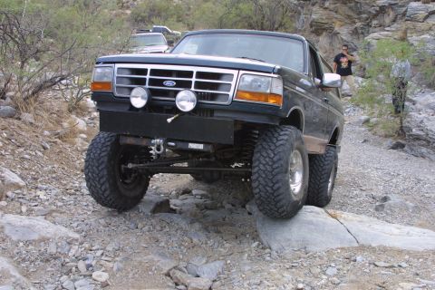 1994 Ford Bronco - This modified Ford Bronco navigates a rocky off-road path, demonstrating its capability on challenging terrain.