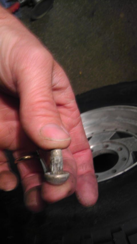 1989 Ford Bronco - Close-up of a hand holding a metal fastener, with a tire and wheel visible in the background.