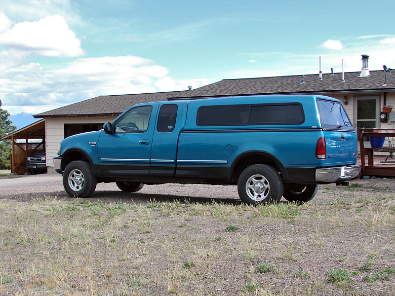 Blue pickup truck with a camper shell parked in a driveway