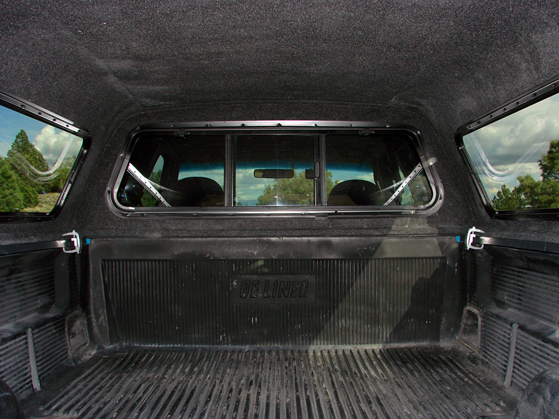 Truck bed interior with topper, showing "DE LINER" text and side windows