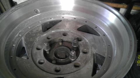 1989 Ford Bronco - Rear face of an unmounted 8-lug aluminum wheel with triangular spoke cutouts, hub and protruding lug studs.