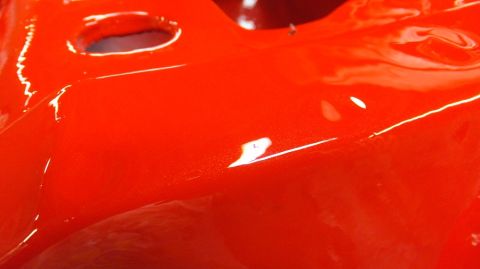 1983 Ford Bronco - A close-up view of a bright red painted metal component, showing its glossy finish and some minor imperfections.
