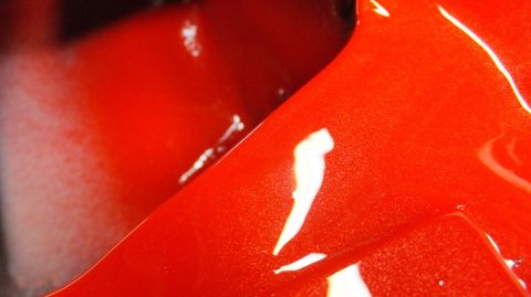 1983 Ford Bronco - Close-up of a shiny red painted metal surface, likely a vehicle part.