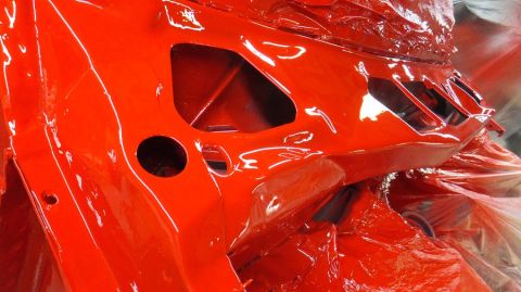 1983 Ford Bronco - The frame of a vehicle is covered in a glossy orange paint, with protective plastic wrap visible.