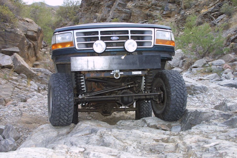 Lifted green Ford on rocks in desert canyon showing exposed solid front axle and driving lights