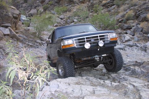 1994 Ford Bronco - A lifted black Ford Bronco navigates a rocky, off-road trail in a desert canyon.