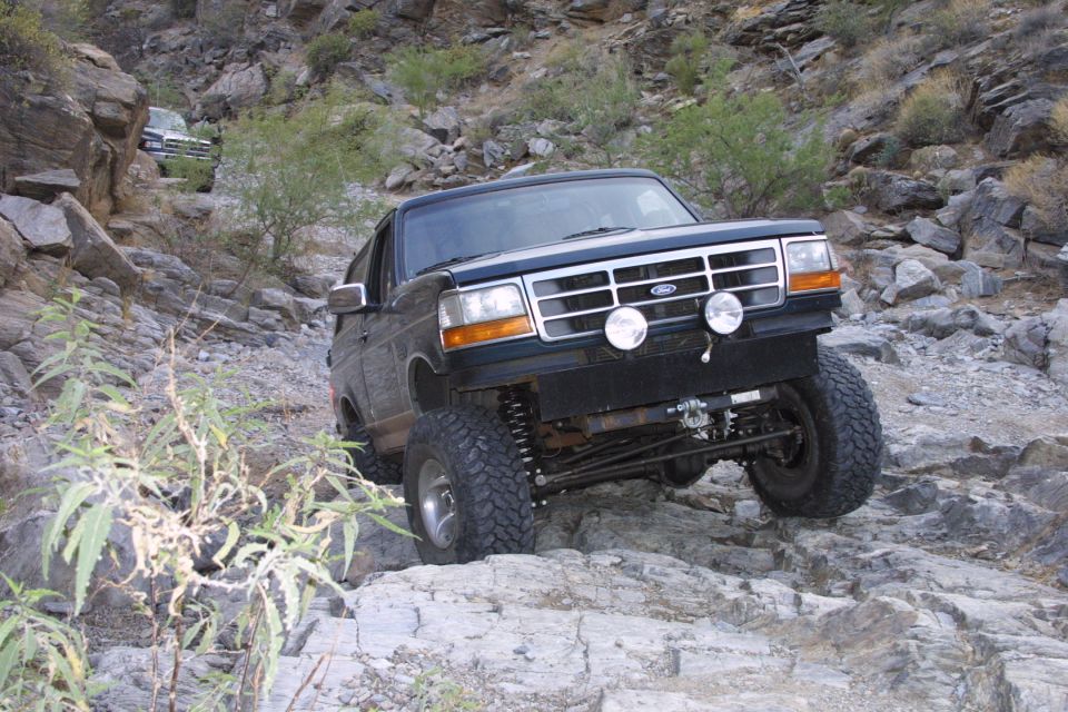 Dark green Ford Bronco flexing over rock ledge in a desert canyon with exposed coil suspension