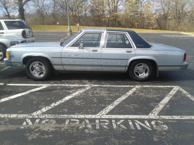 Light blue sedan with dark vinyl top parked sideways over painted NO PARKING area in a lot
