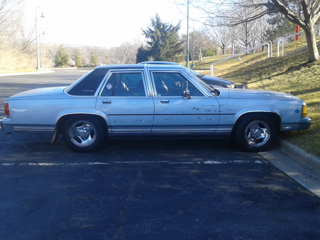 Light blue 1989 Ford Crown Victoria LTD sedan side view with dark vinyl roof and chrome wheels in a parking lot