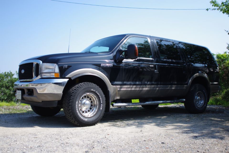 Black Ford Excursion SUV, front three-quarter view on gravel lot with all-terrain tires