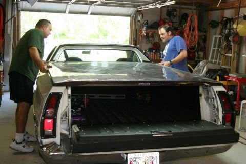 1976 Ford Ranchero - Two men work on closing the bed cover of a 1976 Ford Ranchero inside a garage.