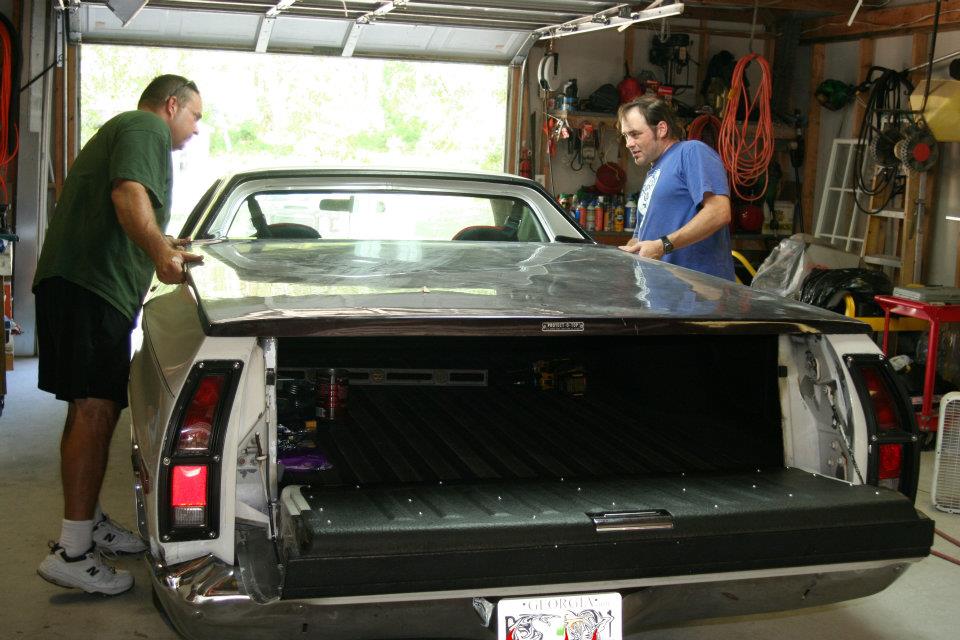 1976 Ford Ranchero bed cover closed by two men in a garage