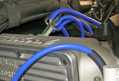 1990 Ford Bronco - Tight engine-bay shot of a cast-aluminum Edelbrock valve cover with blue spark plug wires routed over it and clipped into a metal wire sepa…