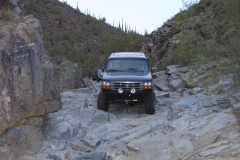 1994 Ford Bronco - A black Ford Bronco navigates a rocky trail in a desert canyon, with another vehicle following.