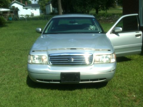 1999 Ford Crown Victoria - A silver sedan sits in a grassy yard with its front passenger door ajar.