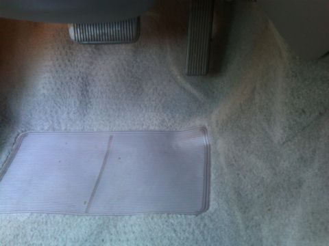 1999 Ford Crown Victoria - The interior floor of a vehicle, showing the pedals and a clear protective floor mat.