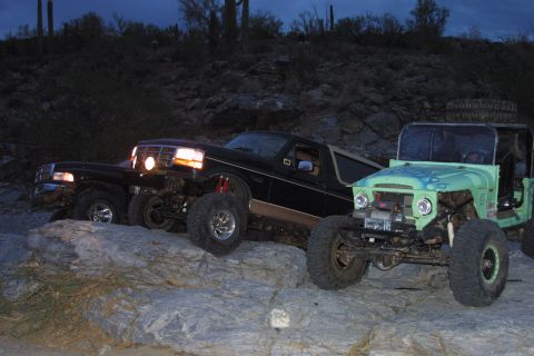 1994 Ford Bronco - Two modified off-road vehicles navigate rocky terrain under a twilight sky.