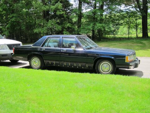 1991 Ford LTD Crown Victoria - A dark blue sedan is parked on a grassy area next to a white SUV.