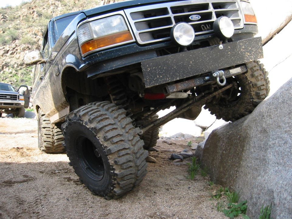 Lifted dark 1990s Ford 4x4 flexed on desert rocks showing mud tires, steel bumper and driving lights
