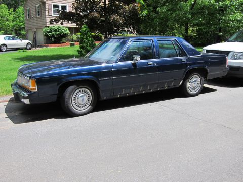 1991 Ford LTD Crown Victoria - A dark blue sedan is parked on the street next to a white SUV.
