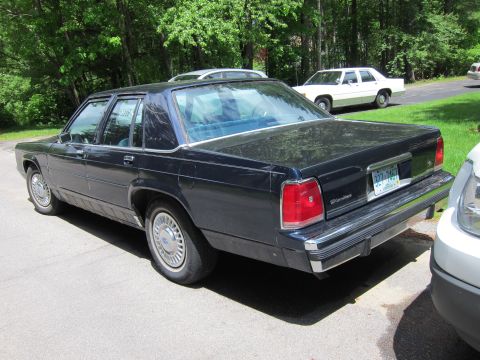 1991 Ford LTD Crown Victoria - A dark blue Ford Crown Victoria sedan is parked on an asphalt surface with trees in the background.
