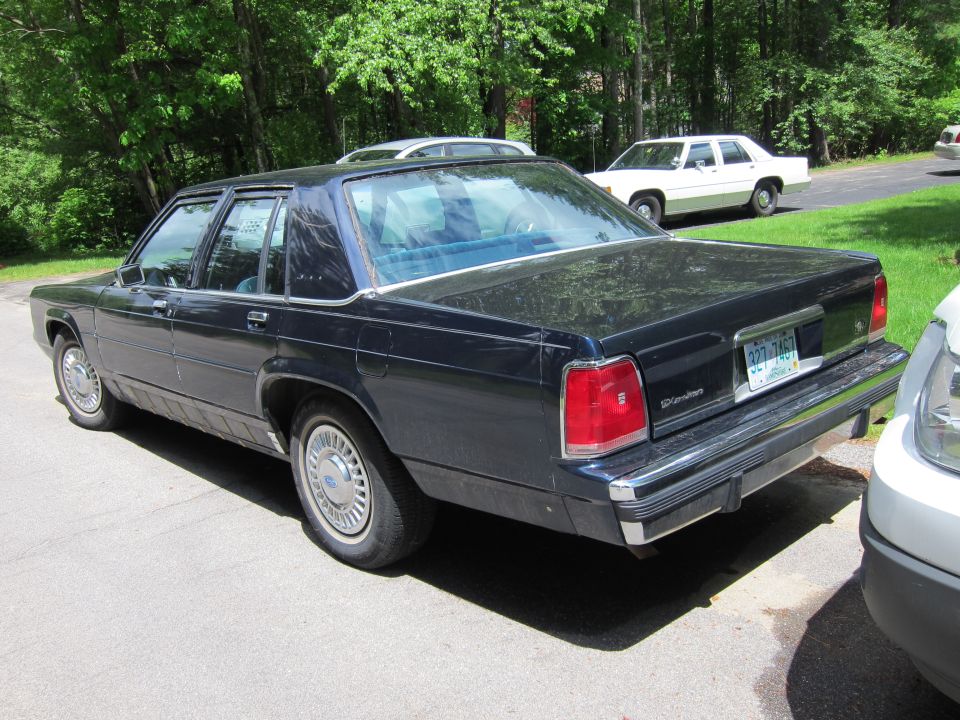 Dark blue Ford Crown Victoria sedan parked on asphalt, rear 3/4 view. License plate visible