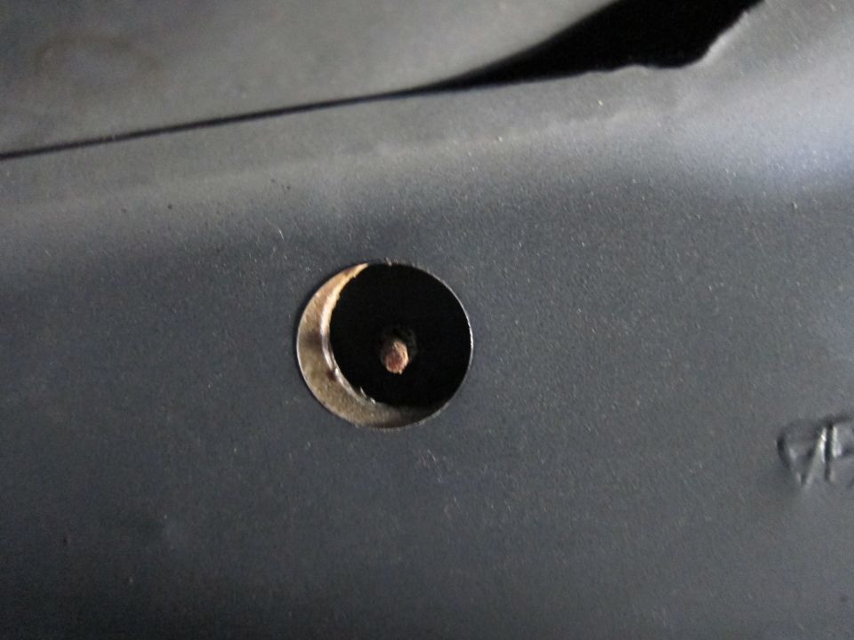 Close-up of a circular hole with a screw visible inside, on a dark textured surface