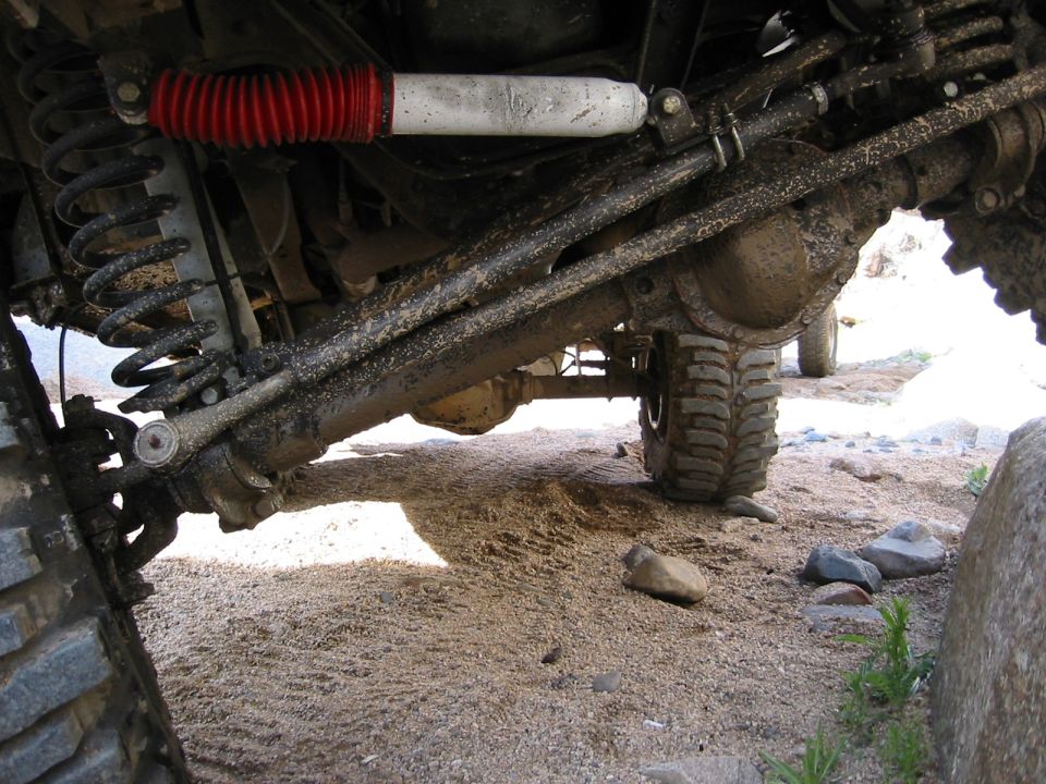 Under-vehicle solid front axle with coil spring, red-boot shock, and muddy tire