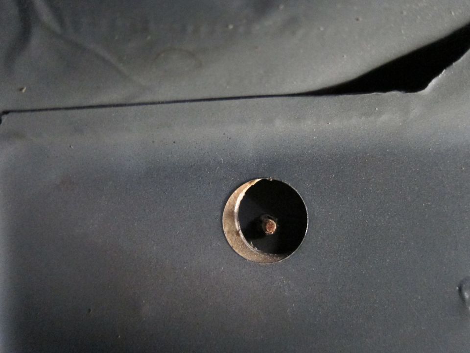 Close-up of a circular hole with a bolt in a dark gray metal panel