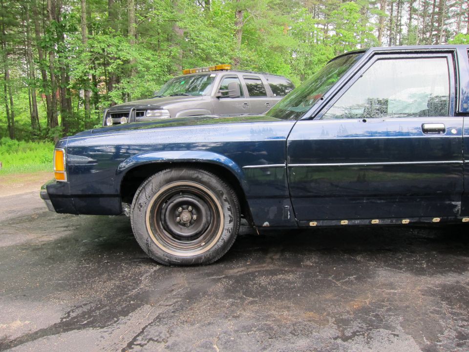 Dark blue 1991 Ford Crown Victoria LTD sedan, front quarter panel and side visible, showing a dented fender and worn tires