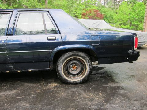 1991 Ford LTD Crown Victoria - Side profile of a dark blue sedan, showing its rear wheel and fender.