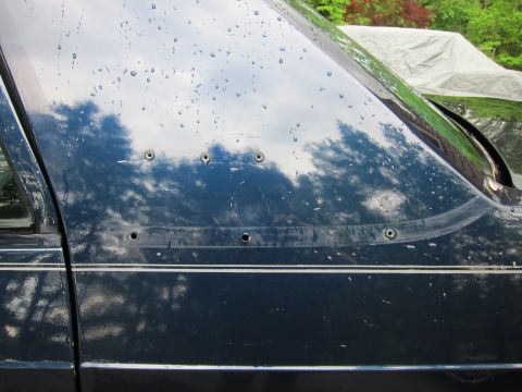 1991 Ford LTD Crown Victoria - Close-up of a dark blue car door showing damage from multiple bullet impacts.