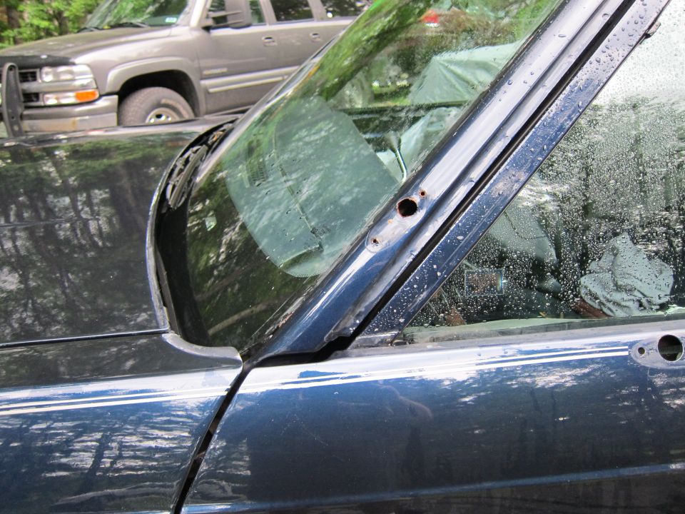 Dark blue sedan door and window frame, with a gray SUV behind it