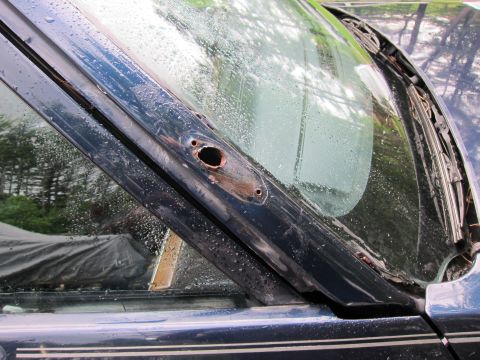 1991 Ford LTD Crown Victoria - Close-up of damaged windshield trim on a dark blue vehicle, showing rust and a hole.